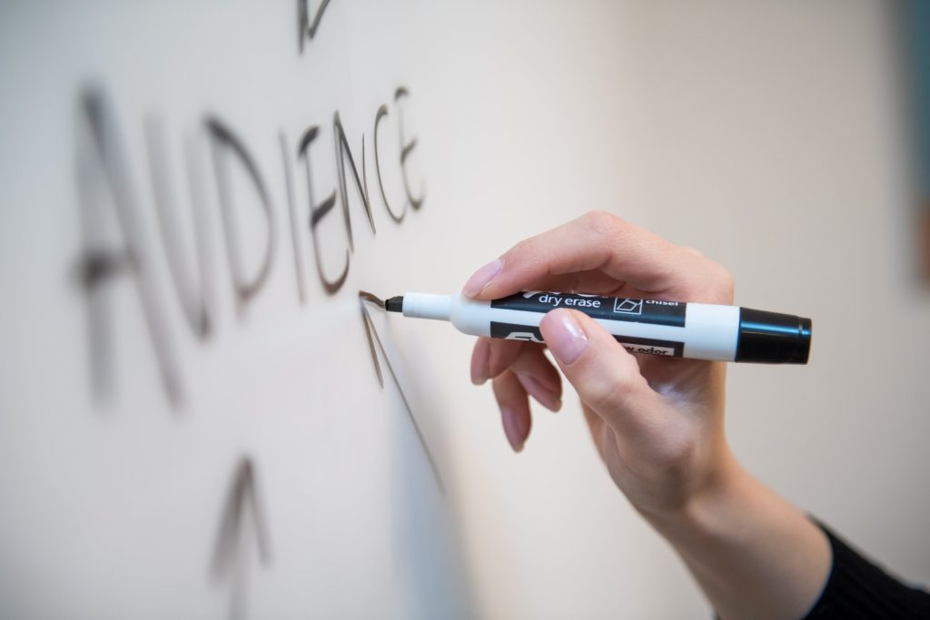 a woman writing the word "audience" on a board