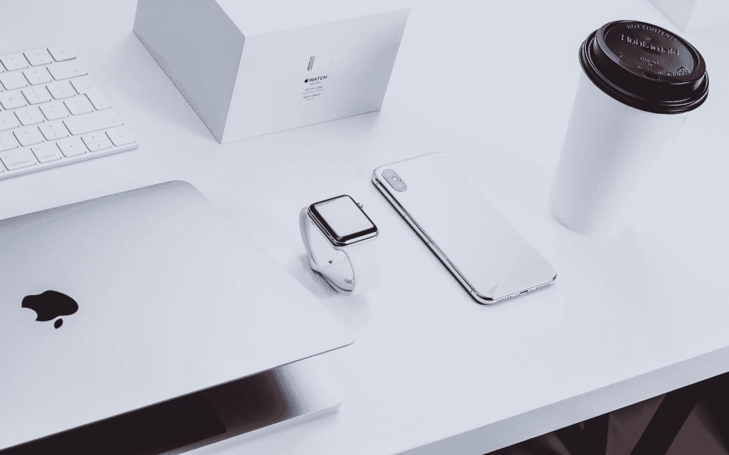apple products: keyboard, macbook, apple watch and iphone on a white desk